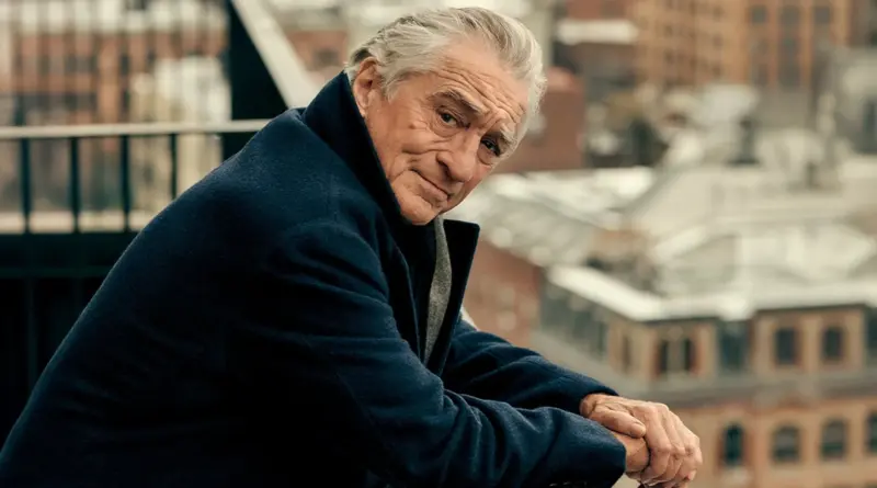 Fotografía de Robert De Niro apoyado en una barandilla con un paisaje urbano de fondo.