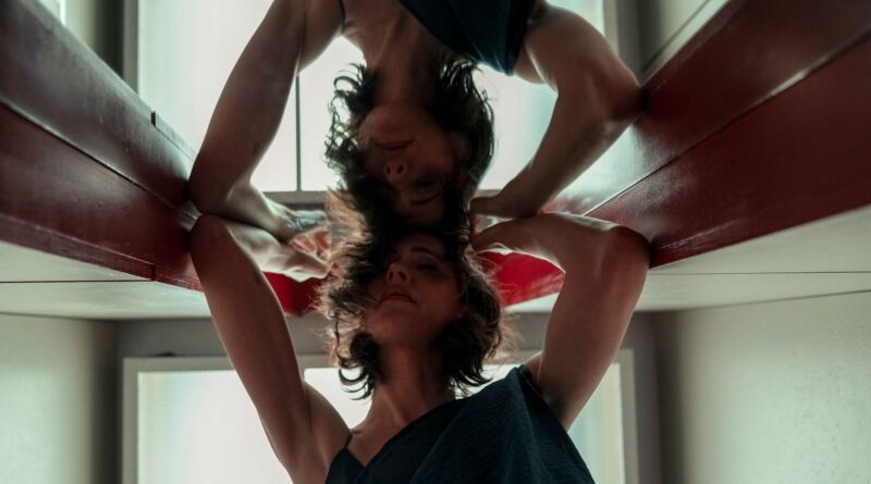 Primer plano de una mujer joven con el cabello corto y oscuro reflejada en una superficie brillante en una composición simétrica invertida.