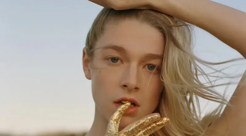 Primer plano de Hunter Schafer con los dedos cubiertos de pan de oro cerca de su boca.