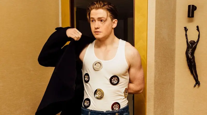 El actor Kit Connor vistiendo una camiseta de tirantes blanca con adornos metálicos circulares.