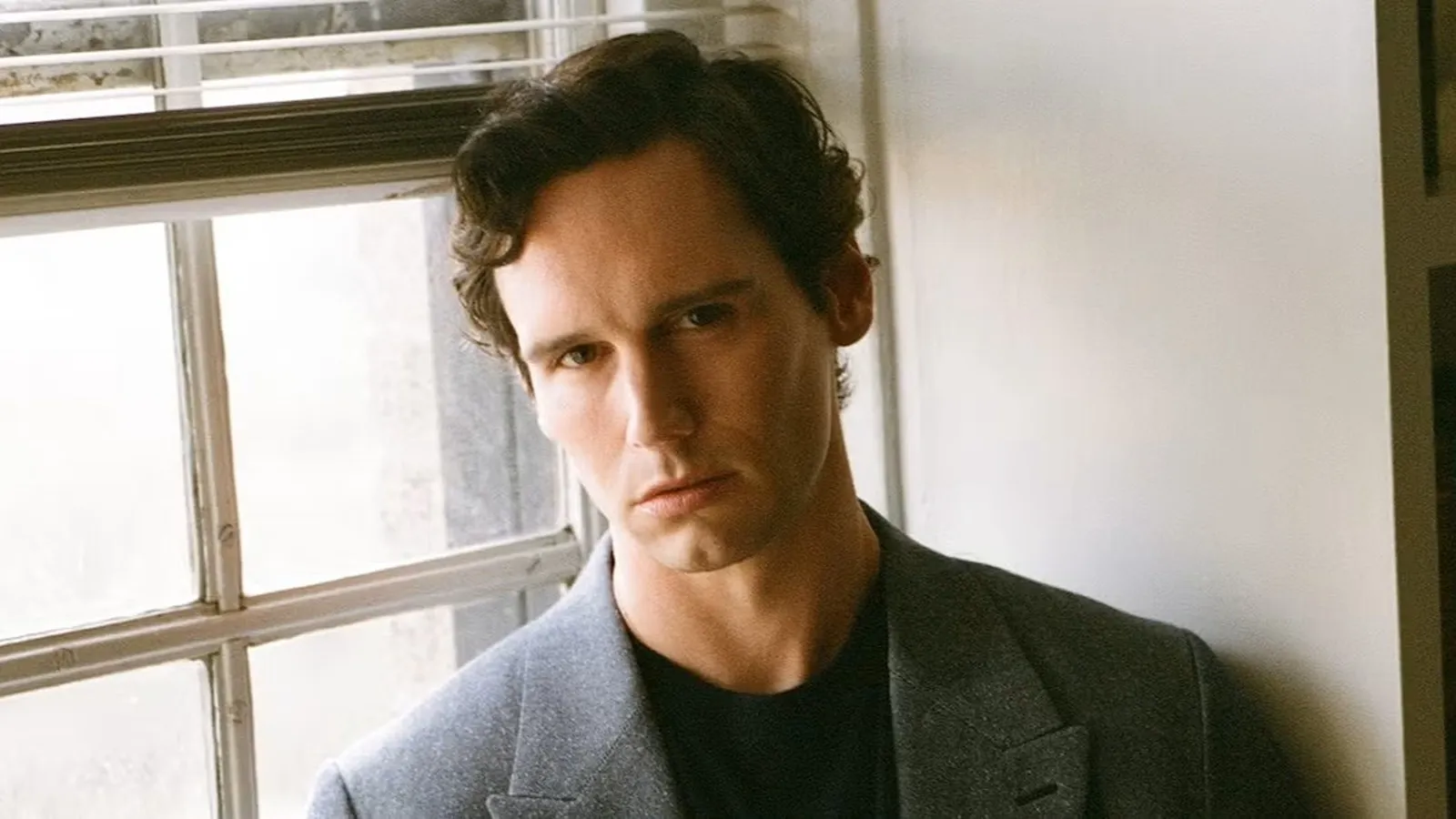 Retrato del actor Cory Michael Smith apoyado en una ventana.