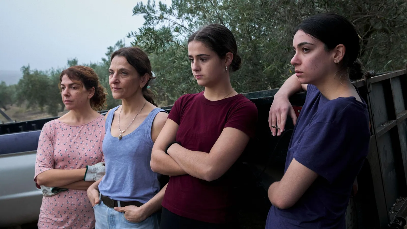 Fotografía de la película Los tortuga que muestra a cuatro mujeres de diferentes edades en un entorno rural al aire libre. Están de pie junto a la parte trasera de una furgoneta o remolque, mirando hacia la izquierda con expresiones de cansancio y resignación. Visten ropa sencilla de diario, como camisetas de tirantes y de manga corta, bajo un cielo nublado y grisáceo.