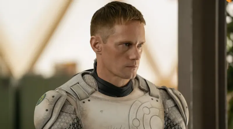 El actor Alexander Skarsgård, interpretando a un robot con armadura futurista blanca y gris, con una expresión seria y el cabello rubio corto, mirando hacia un lado.