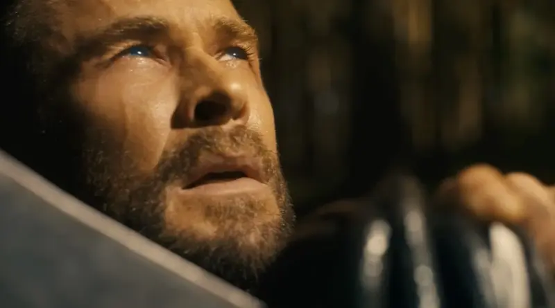 Primer plano cinematográfico de Chris Hemsworth como Thor en el teaser de "Vengadores: Doomsday". Se le ve con la mirada dirigida hacia arriba, ojos brillantes y expresión de vulnerabilidad y súplica. La iluminación es cálida y lateral, resaltando su barba y facciones en un entorno oscuro y desenfocado.