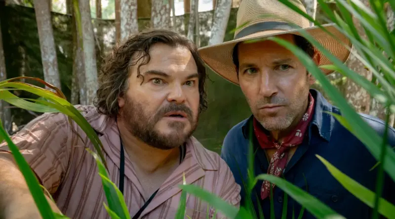 Fotograma de la película 'Anaconda' (2025). En primer plano, los actores Jack Black y Paul Rudd miran a través de la densa vegetación de la selva con expresiones de asombro y cautela. Jack Black, a la izquierda, lleva una camisa de rayas rosadas y luce barba y cabello alborotado. A la derecha, Paul Rudd viste una camisa azul, un pañuelo rojo al cuello y un sombrero de paja de estilo explorador.