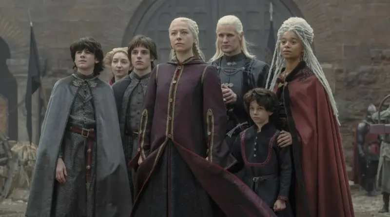 Fotograma de 'La Casa del Dragón'. Plano medio de Rhaenyra Targaryen (Emma D'Arcy) con expresión solemne, rodeada por Daemon Targaryen y sus hijos Jacaerys, Lucerys y las gemelas Baela y Rhaena, todos mirando hacia el cielo con preocupación en un exterior de piedra gris.