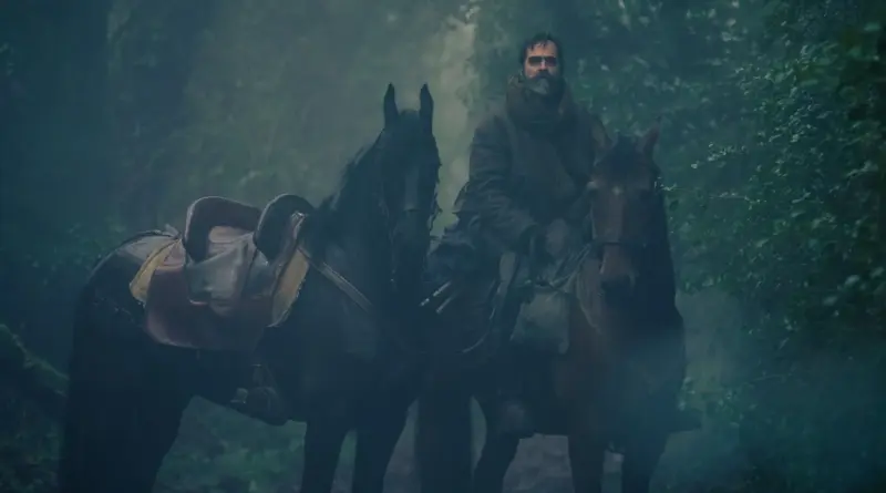 Fotograma de 'Lobo'. Luis Tosar, caracterizado con una densa barba canosa y ropas de época desgastadas, monta a caballo en medio de un bosque verde cubierto de niebla espesa, sosteniendo las riendas de un segundo caballo sin jinete a su lado.