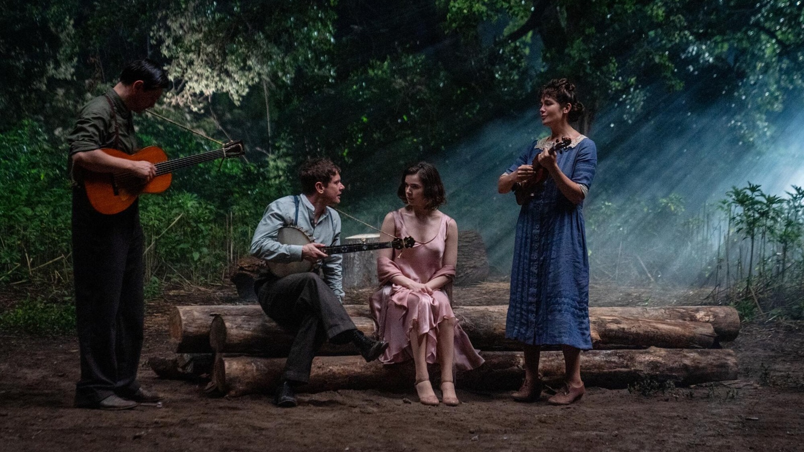 Fotograma atmosférico nocturno de 'Los pecadores' en un claro del bosque con neblina y rayos de luz filtrándose entre los árboles. Cuatro personajes están reunidos tocando música: a la izquierda, un hombre de pie toca una guitarra acústica; en el centro, sentados sobre un tronco, un hombre toca un banjo mirando a una mujer con vestido rosa de seda; a la derecha, otra mujer de pie toca el violín. Visten ropa de época rural de los años 30.