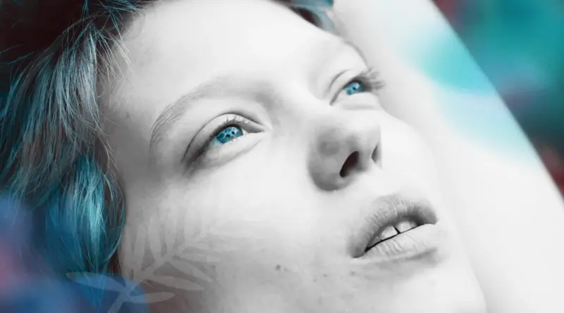 Primerísimo primer plano del rostro de la actriz Léa Seydoux con el cabello teñido de azul y corte corto. Mira hacia arriba con ojos llorosos y vidriosos. Sobre la imagen, en la esquina inferior izquierda, se percibe una marca de agua translúcida con la hoja de palma del Festival de Cannes.