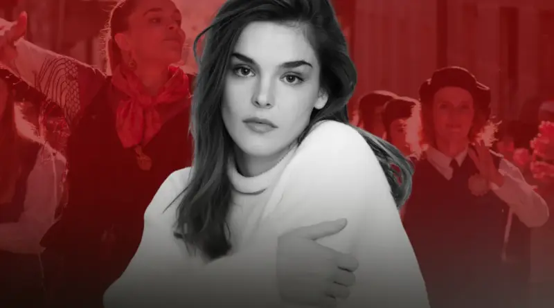 Composición gráfica estilo collage. En primer plano, un retrato recortado en blanco y negro de la actriz Judith Fernández, quien mira fijamente a la cámara con expresión serena y profunda, vestida con un jersey blanco de cuello alto y abrazándose a sí misma. El fondo está teñido completamente de rojo intenso y muestra imágenes superpuestas de la película 'Rondallas': a la izquierda, ella misma bailando con el traje tradicional, y a la derecha, otros miembros de la rondalla aplaudiendo.