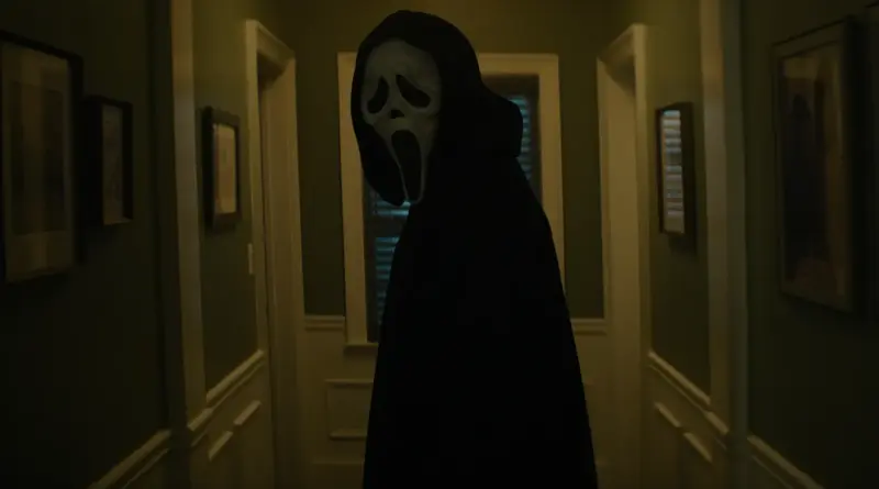 Ghostface de perfil en un pasillo doméstico estrecho con paredes verdes, girando la cabeza hacia la cámara en una postura de acecho silencioso. en 'Scream 7'