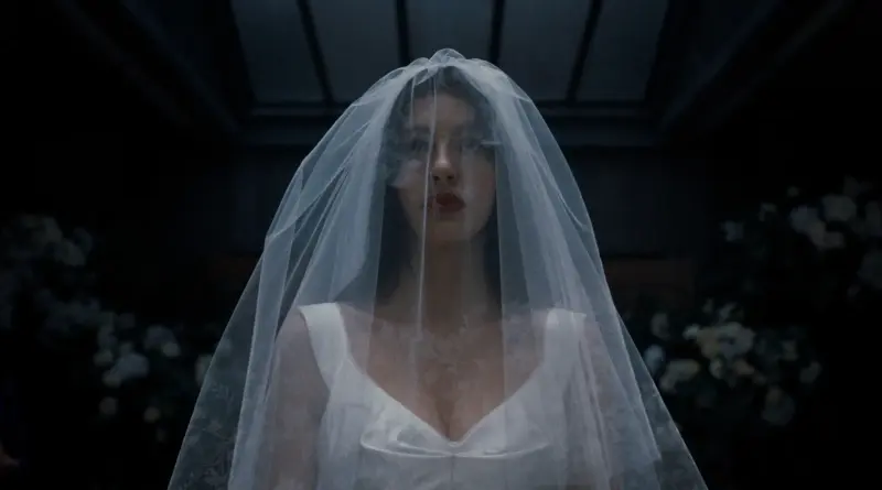 'Algo terrible está a punto de suceder' lanza un tráiler que te quitará las ganas de casarte. 1 Fotograma De 'Algo Terrible Está A Punto De Suceder'. Plano Frontal Simétrico De Una Novia Vestida De Blanco En Una Habitación Oscura. Un Velo De Tul Cubre Completamente Su Rostro Y Torso, Dándole Un Aspecto Fantasmal Y Estático Bajo Una Luz Cenital Fría.