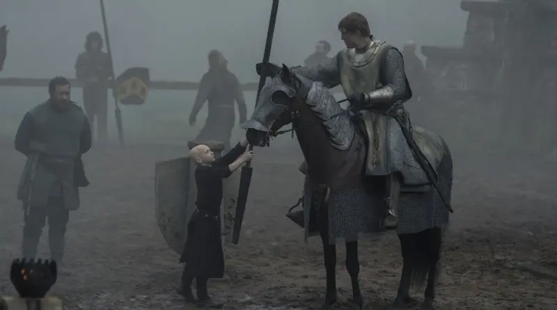 Fotograma De 'El Caballero De Los Siete Reinos'. Escena Del Juicio De Siete Envuelta En Niebla Gris. Ser Duncan El Alto, Con Armadura Completa, Está Montado En Un Caballo Oscuro. El Pequeño Egg (Calvo Y Vestido De Negro) Le Entrega Una Lanza Larga Mirándole Hacia Arriba. Al Fondo Se Ven Otros Caballeros Y Estandartes Difuminados.