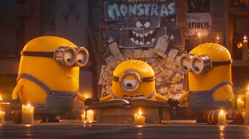 Fotograma de 'Minions & Monsters'. Tres Minions se cogen de la mano en círculo alrededor de un libro abierto sobre una mesa iluminada por velas. Detrás de ellos, un decorado casero de cartón muestra un dibujo infantil de un monstruo y el texto "MINIONS MONSTRAS".