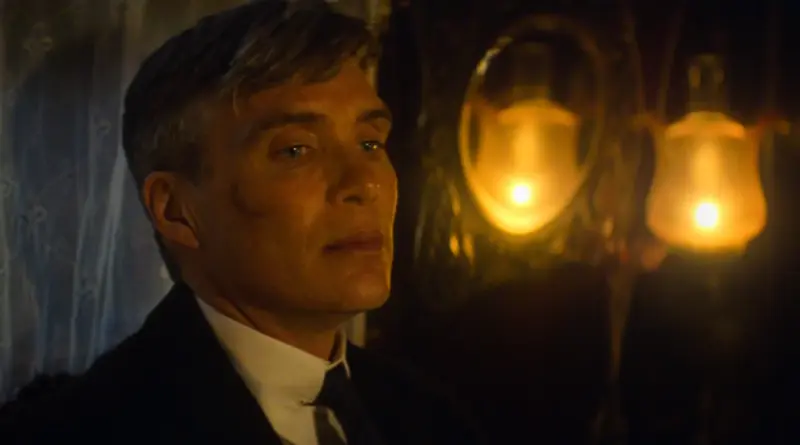 Fotograma De 'Peaky Blinders: El Hombre Inmortal'. Primer Plano De Perfil De Tommy Shelby En Una Habitación Oscura, Iluminada Solo Por La Luz Cálida De Una Lámpara De Gas O Vela Que Se Refleja En Un Espejo Antiguo Detrás De Él. Su Mirada Está Perdida, Cansada Y Melancólica, Con El Pelo Grisáceo Visible Bajo El Corte Undercut.