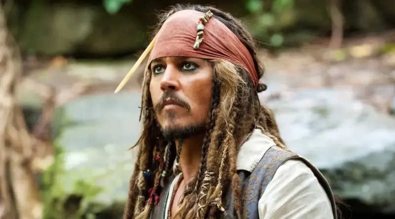 'Piratas del Caribe 6' se haría realidad con el hijo de Jack Sparrow y Margot Robbie, pero el regreso de Johnny Depp sigue siendo una incógnita. 1 Fotograma de la saga 'Piratas del Caribe' que nos hace pensar en 'Piratas del Caribe 6'. Primer plano de Johnny Depp como Jack Sparrow en un entorno selvático desenfocado. Luce su característico pañuelo rojo en la cabeza, maquillaje de ojos oscuro (kohl), un hueso decorativo en el cabello y abalorios trenzados en la barba, mirando hacia arriba con expresión pensativa.