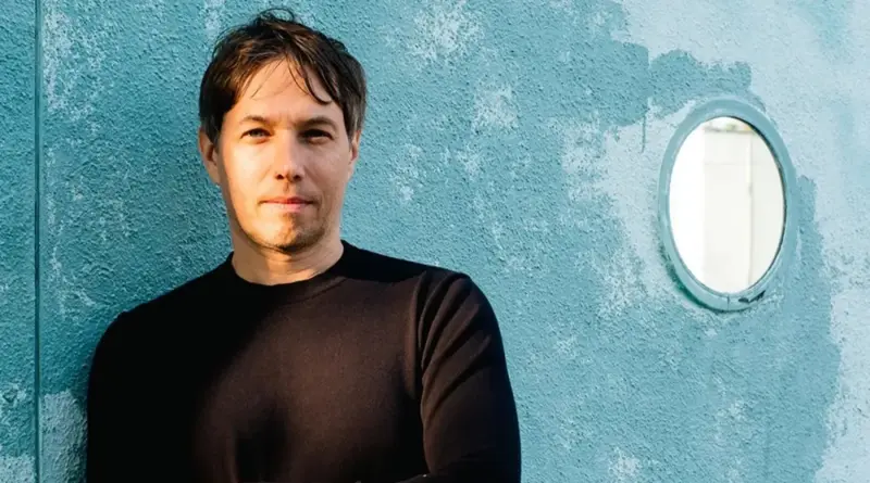 Primer plano del director de cine Sean Baker frente a una pared azul.
