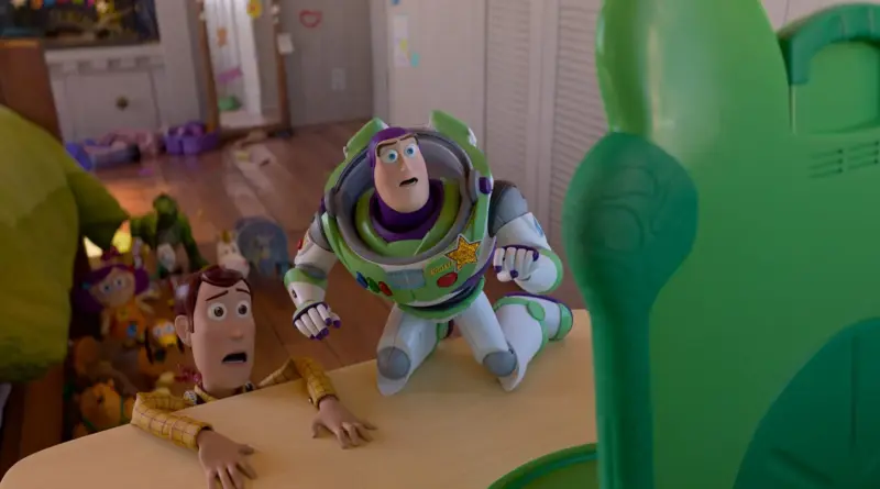 Fotograma De 'Toy Story 5'. Woody Y Buzz Están Agachados Sobre Una Mesa De Madera, Mirando Hacia Arriba Con Asombro. Frente A Ellos Se Ve El Reverso De La Funda Verde De La Tablet Lillypad, Que Se Alza Como Un Monolito Gigante Ante Los Pequeños Juguetes.