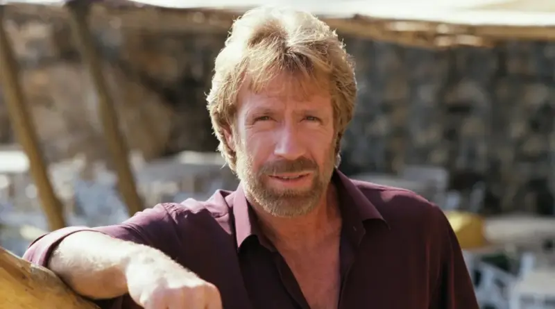 Retrato De Primer Plano De Chuck Norris Con Camisa Granate Y Barba Frente A Un Fondo Exterior Desenfocado.