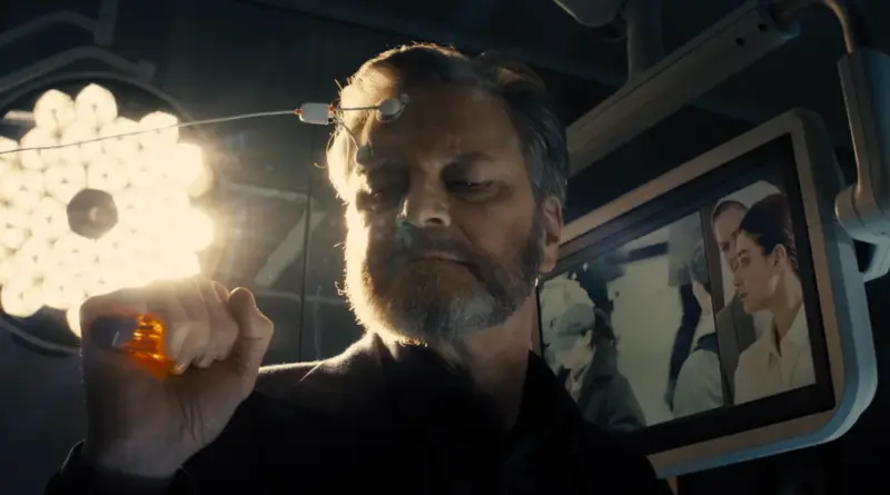 Fotograma De 'El Día De La Revelación'. Colin Firth Con Sensores En La Cabeza En Un Laboratorio Tecnológico Frente A Una Pantalla Con Imágenes Médicas.