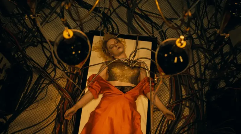 Fotograma De '¡La Novia!' ('The Bride!'). Plano Cenital De La Novia Tumbada E Inconsciente Sobre Una Plancha Blanca, Conectada A Gruesos Tubos Y Cables.