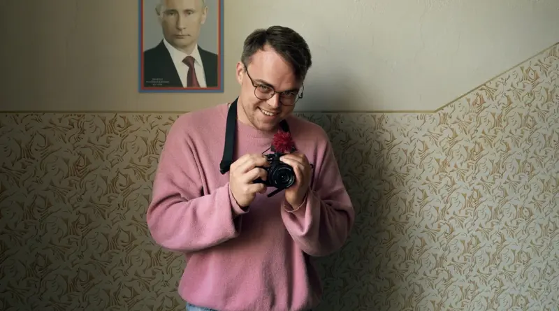 Un Hombre Con Cámara Sonriendo Frente A Un Retrato De Vladimir Putin En Mr. Nobody Contra Putin.