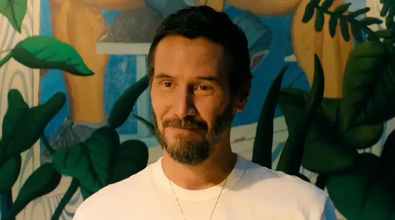 Keanu Reeves Sonriendo Con Una Camiseta Blanca Frente A Un Mural Colorido En Una Escena De Outcome.