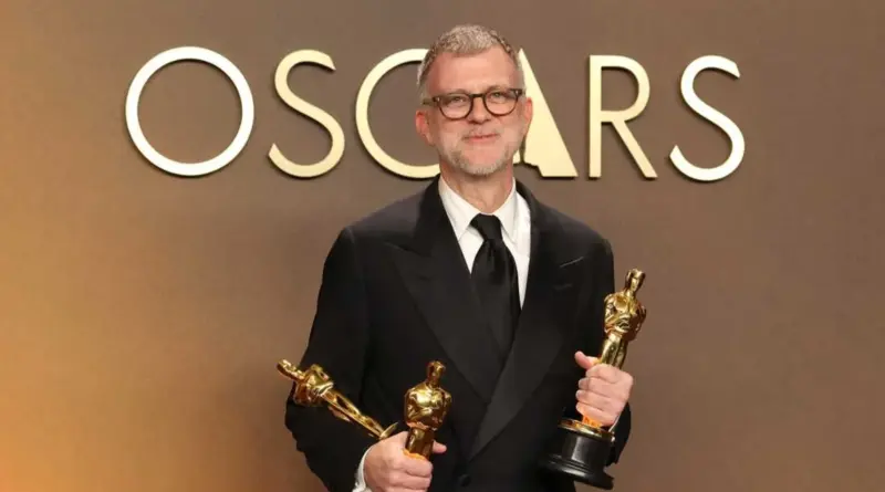 Paul Thomas Anderson Sonriendo Con Tres Estatuillas De Los Premios Oscar 2026 Frente Al Logotipo De La Academia.
