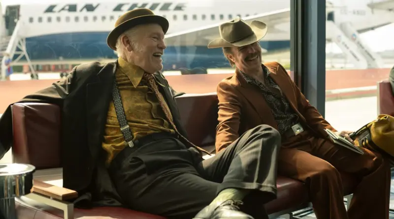 Fotograma De La Película &Quot;Wild Horse Nine&Quot;. Dos Hombres Con Vestimenta Retro Riendo Alegremente En La Sala De Espera De Un Aeropuerto, Con Un Avión De Lan Chile De Fondo A Través De Un Ventanal.