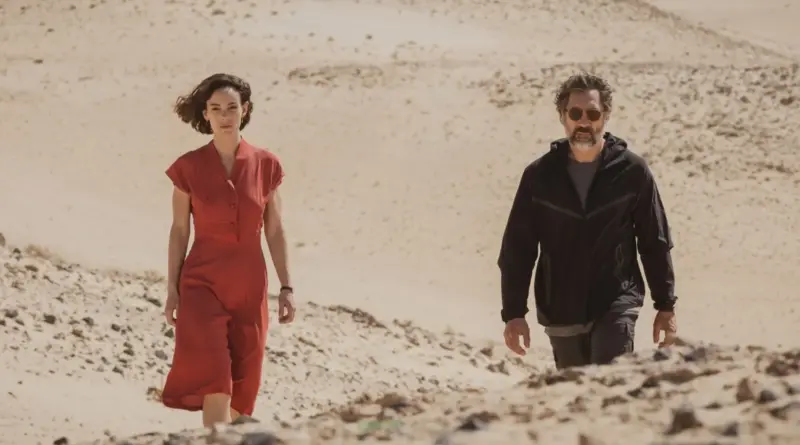 Victoria Luengo Con Vestido Rojo Y Javier Bardem De Negro Caminando Por Dunas De Arena En El Ser Querido.
