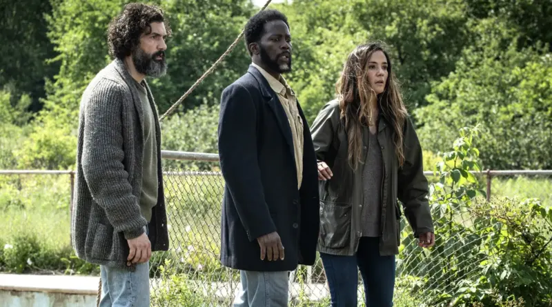 Protagonistas De La Serie From Observando Algo Con Preocupación Cerca De Una Valla Metálica.