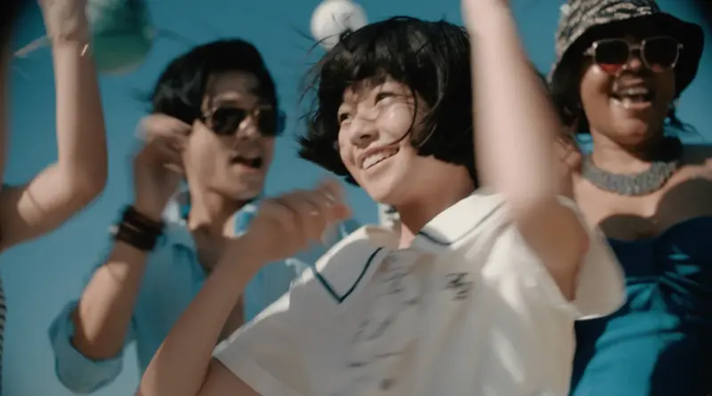 La joven protagonista de Renoir baila sonriendo junto a otras personas bajo un cielo azul despejado.