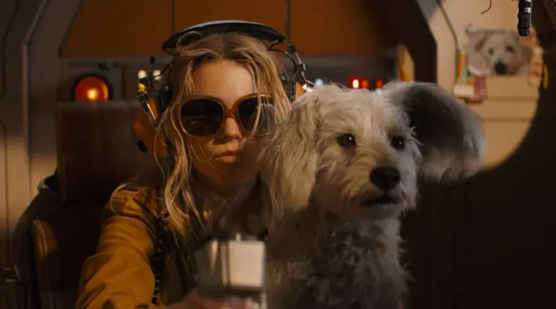 Kara Zor-El Con Gafas De Sol Y Auriculares Sentada Junto A Un Perro Blanco (Krypto).