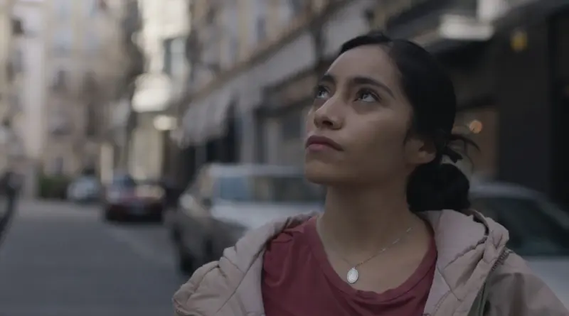 Fotograma de la película Ceniza en la boca: una mujer joven mirando hacia el cielo en una calle urbana.
