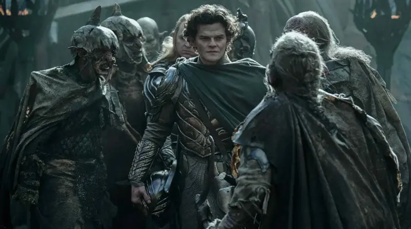 Elfo Elrond con armadura y capa verde, rodeado y confrontado por un grupo de orcos con cascos deteriorados, en El Señor de los Anillos: Los Anillos de Poder.