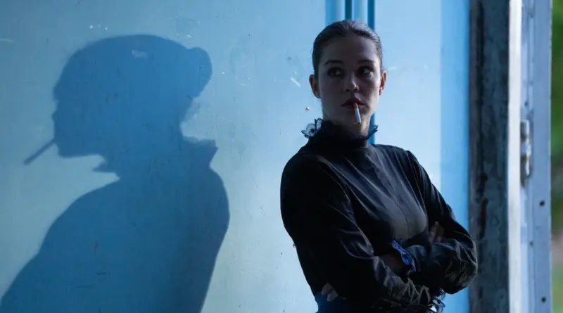Fotografía de la película Garance en el Festival de Cannes 2026: Una mujer con un cigarrillo en la boca y los brazos cruzados viste un traje oscuro de época frente a una pared azul claro donde se proyecta su silueta en sombra.