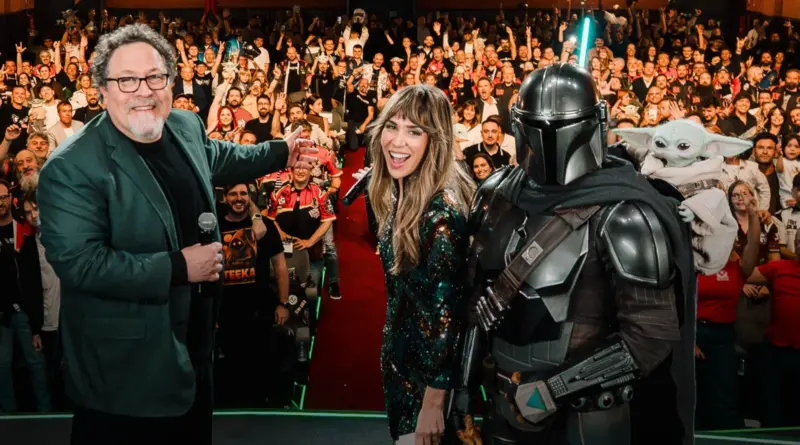 Jon Favreau, una presentadora y una persona disfrazada del Mandaloriano con Grogu en el escenario frente a un público entusiasta en la presentación de Madrid de 'The Mandalorian and Grogu'.