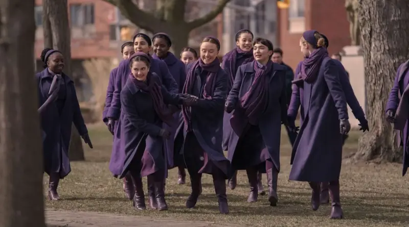 Escena de la serie Los testamentos en la que un grupo de mujeres jóvenes camina sonriente al aire libre vistiendo abrigos morados y diademas.