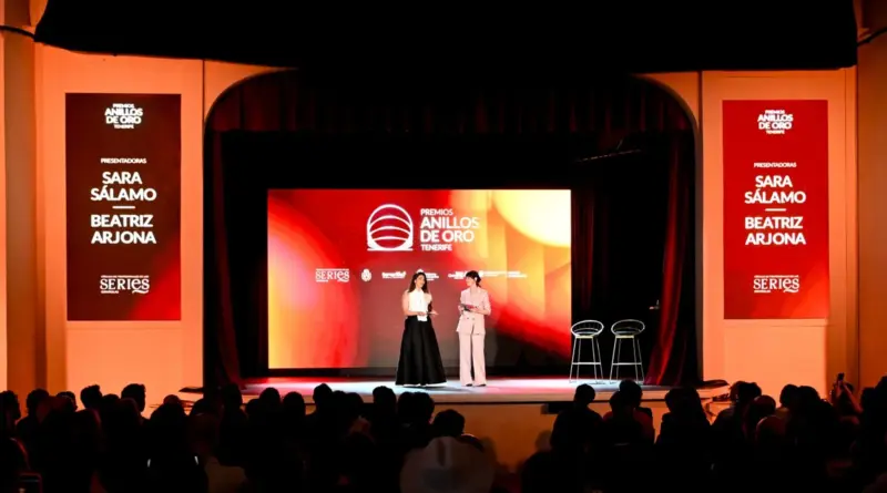 Dos presentadoras en el escenario de los Premios Anillos de Oro Tenerife, frente a una gran pantalla roja y carteles laterales con sus nombres: Sara Sálamo y Beatriz Arjona.