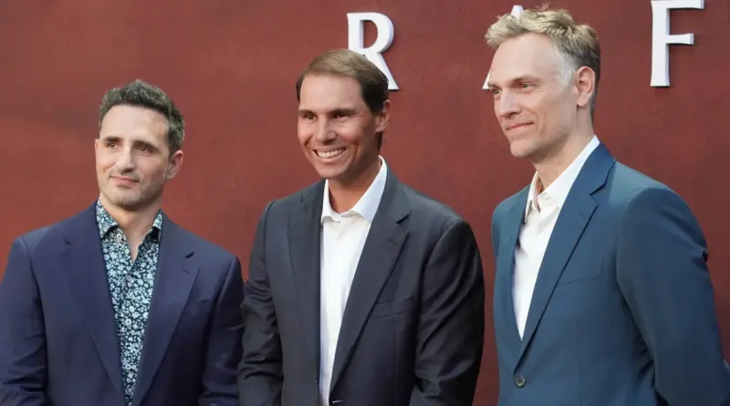De izquierda a derecha, tres hombres sonrientes posan en un photocall de fondo rojo: el primero con traje azul y camisa estampada, Rafael Nadal en el centro con traje oscuro y camisa blanca, y el tercero con traje azul claro y camisa blanca.