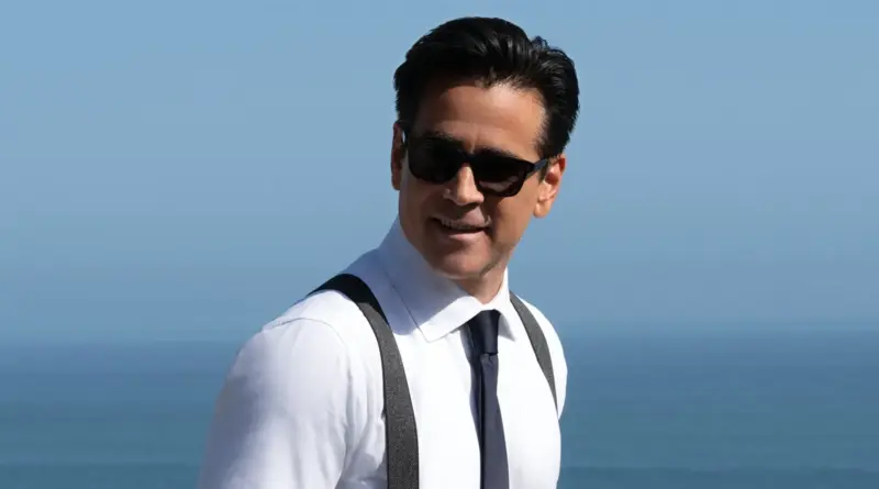Plano medio de Colin Farrell sonriendo con gafas de sol y tirantes frente al mar en la serie Sugar.