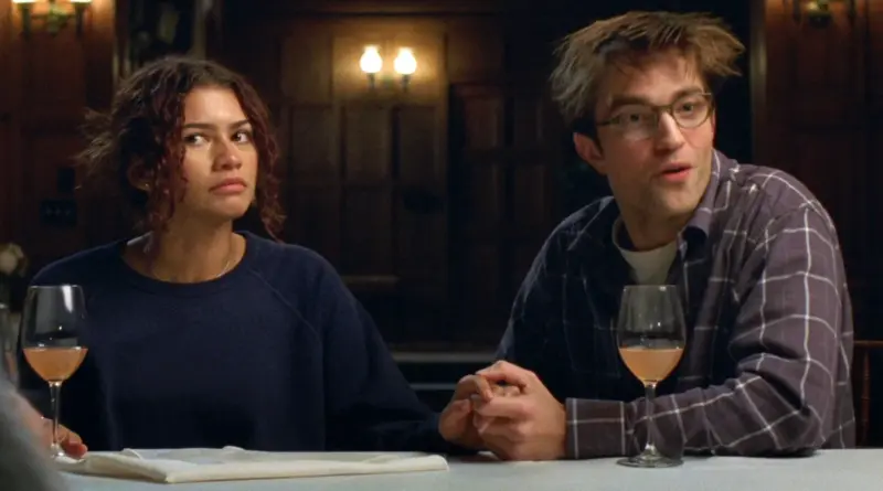 Zendaya y Robert Pattinson sentados a la mesa tomados de la mano en una escena de The Drama.