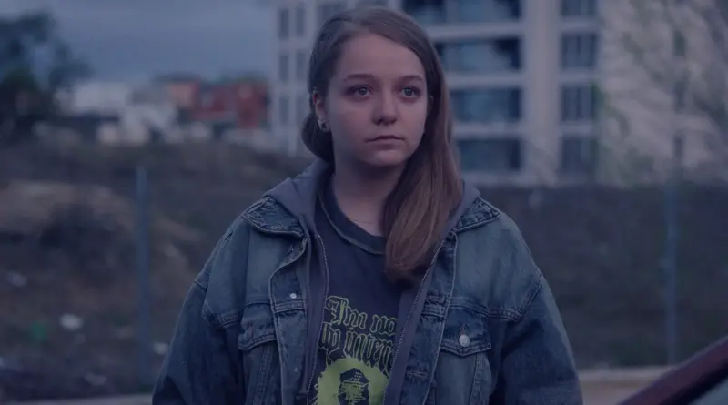 Primer plano de Júlia Mascort en una escena exterior de "Yo no moriré de amor". Viste una chaqueta vaquera y tiene una expresión de desconcierto.