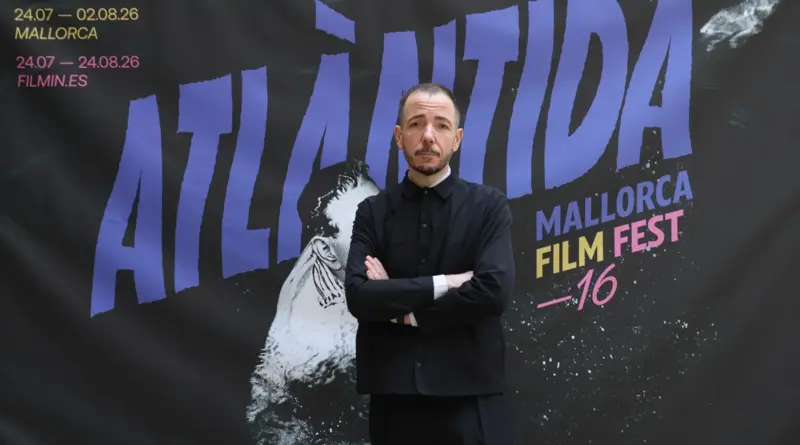 Retrato de un hombre de pie frente a un cartel promocional del Atlàntida Mallorca Film Fest 16.