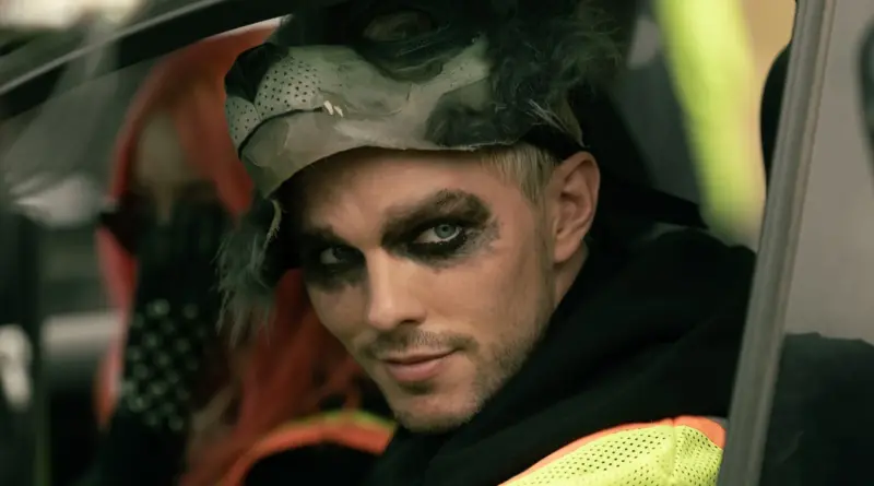 Primer plano de Nicholas Hoult con maquillaje oscuro en los ojos y una máscara de lobo levantada sobre la cabeza en Cómo robar un banco.