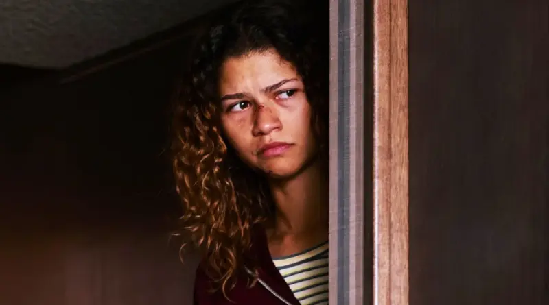 Zendaya asomándose detrás del marco de una puerta con expresión seria y cansada en la serie Euphoria.