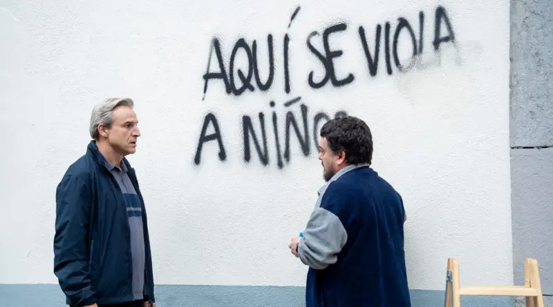 Fotograma de la película La luz. Alberto San Juan conversa en la calle con otro hombre frente a una pared blanca con una pintada de grafiti que denuncia abusos infantiles.