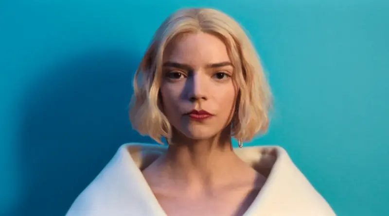 Retrato de estudio de Anya Taylor-Joy para la serie Lucky. Plano medio frontal de la actriz con cabello rubio corto y labios rojos, vistiendo una prenda blanca de cuello ancho, recortada sobre un fondo azul turquesa liso.