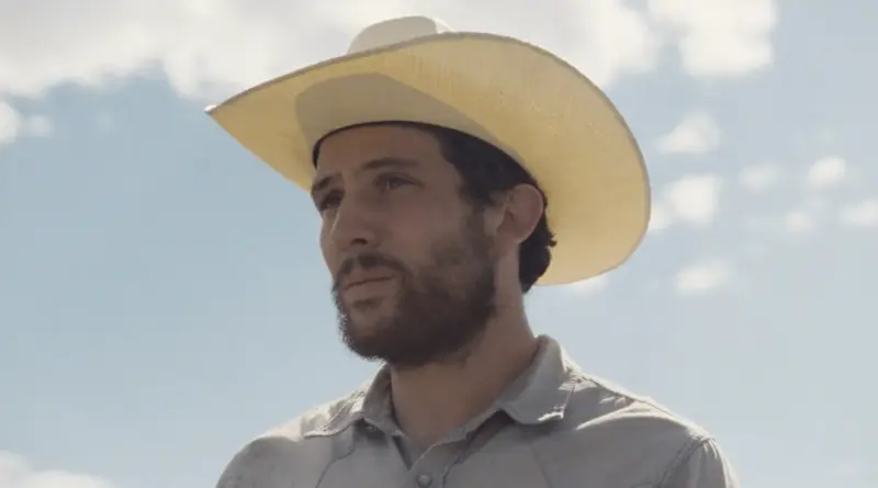 Retrato de perfil del protagonista de la película Rebuilding, un hombre con sombrero de vaquero y barba que mira fijamente hacia el horizonte.