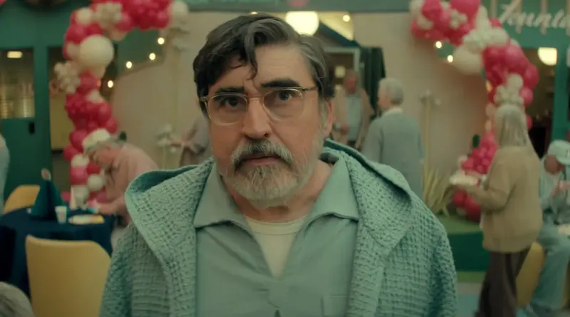 The Boroughs: Jubilación rebelde: un hombre con gafas y cárdigan verde mira fijamente a cámara en una sala de celebración de la serie que no tendrá temporada 2.